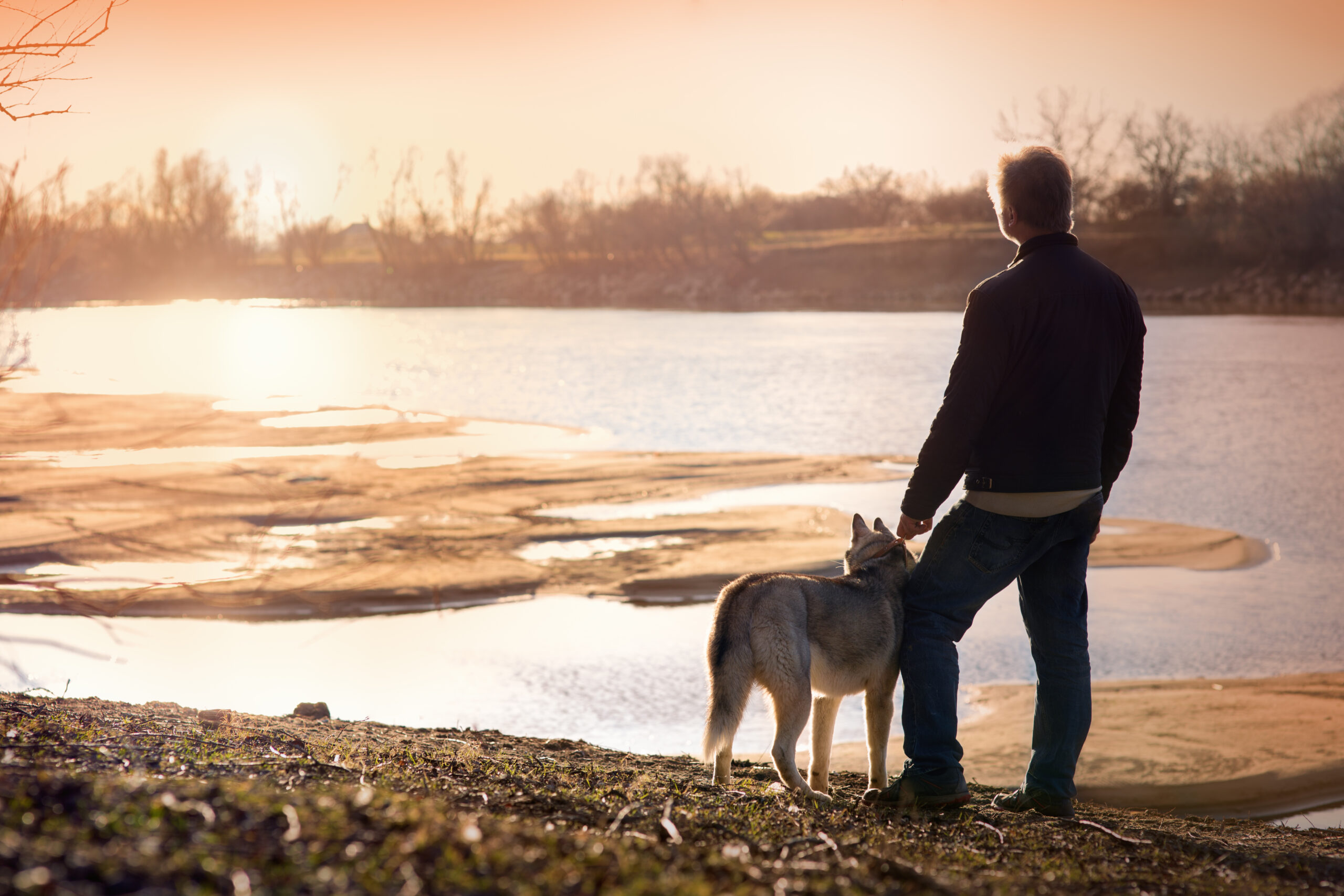A man and his dog standing by the river watching the sunset